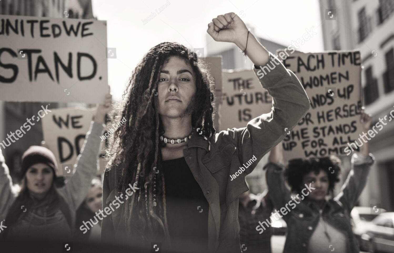 Black and white photograph of a woman at the front line of a protest, holding her first in the air, resolved.